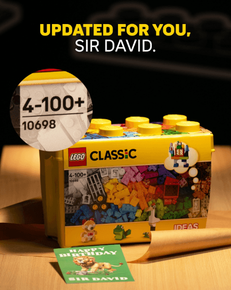 Yellow LEGO Classic box with colorful bricks sits on a wooden table, a birthday card reading 'Happy Birthday Sir David' nearby, and a circular magnified inset showing '4-100+' on the set label.