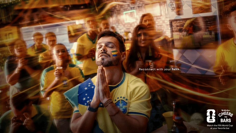 Brazilian football fan with face paint and flag draped over shoulder, eyes closed in prayer among cheering crowd; slogan 'Reconnect with your faith' visible in background.