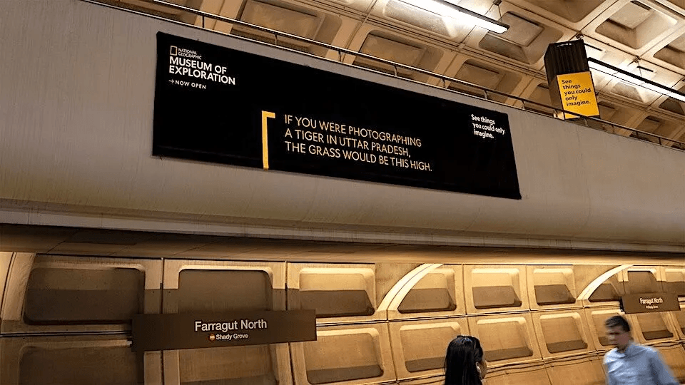 Image – new classic Interior metro concourse with a large National Geographic Museum of Exploration banner; station signs read Farragut North to Shady Grove, with a few commuters nearby.