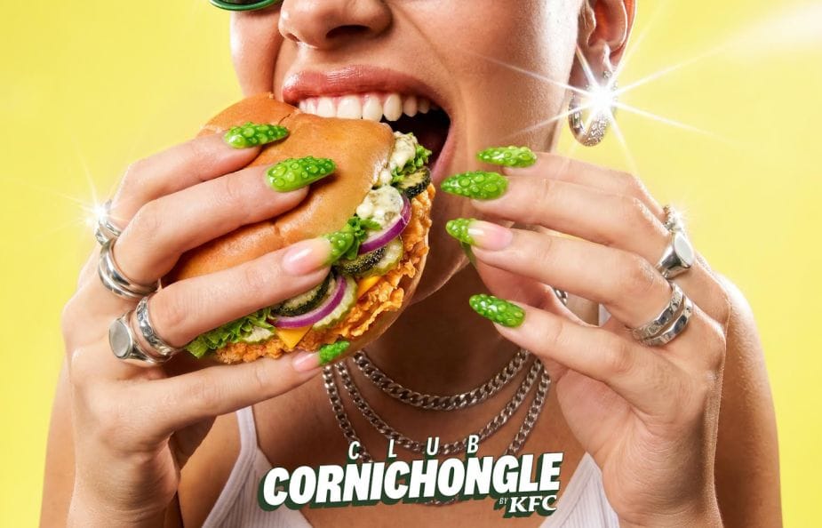 Kfc-pickle-burger5a8woo28 – new classic Woman with bright lime-green nails bites into a chicken burger, showing rings and a yellow background.