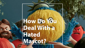 Furry yellow mascot head with blue accents and a Statue of Liberty crown; foreground text asks, 'How Do You Deal With a Hated Mascot?'.